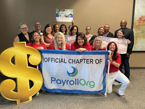A group holding a sign that says 'Official Chapter of PayrollOrg' smiling for NPW